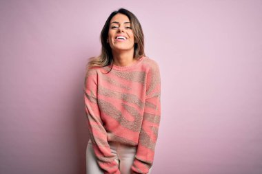 Moda kıyafetleri giyen genç ve güzel bir kadın. Manken, sokak tarzı giyiniyor. Pembe arka planda dikiliyor.