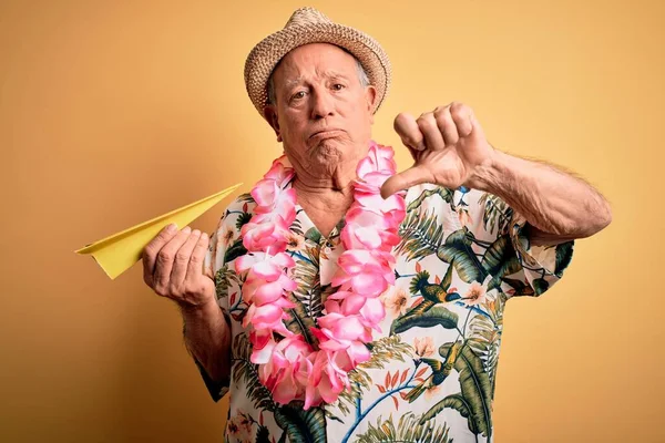 Beyaz saçlı, yaz şapkası takan ve elinde kızgın yüzüyle kağıt uçak tutan Hawaii zambağı olan yaşlı bir adam. Negatif işaretler baş parmakları aşağıda, reddedilme kavramı.