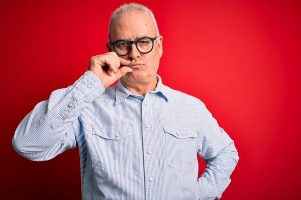 Orta yaşlı yakışıklı beyaz bir adam kırmızı arka planda gözlük takıyor ve dudakları parmaklarıyla kapalı. Gizli ve sessiz, tabu konuşması