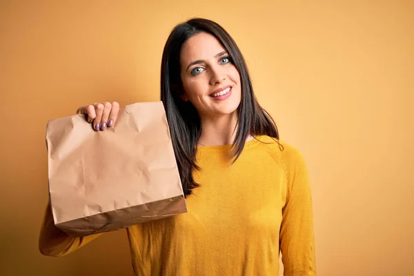 年轻的黑发女人 蓝眼睛 手里拿着装有食物的纸袋 脸上挂着快乐的表情 脸上挂着自信的微笑 露出牙齿 — 图库照片