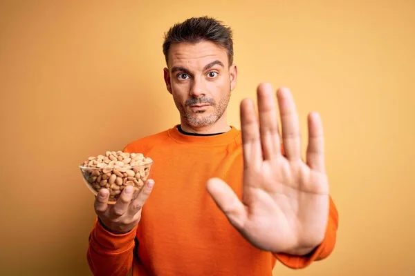 Joven Hombre Guapo Sosteniendo Tazón Con Cacahuetes Sobre Fondo Amarillo — Foto de Stock