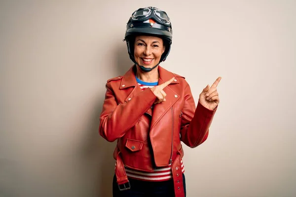中年オートバイの女性身に着けていますオートバイのヘルメットとジャケット上の白い背景笑顔とカメラを見てポインティングで二つの手と指で側面 — ストック写真