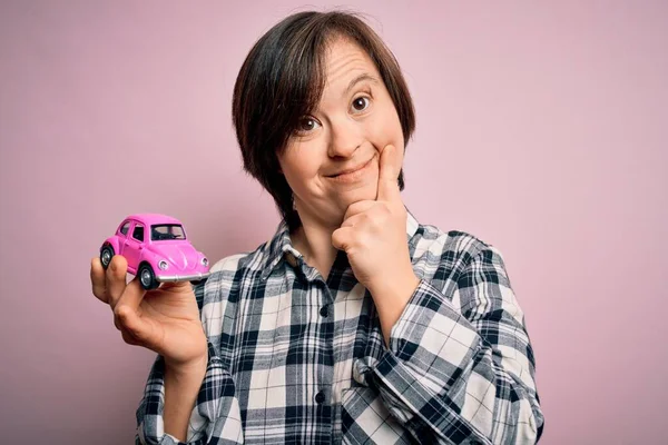 ピンクの背景深刻な顔の上に運転免許証保険として小さな車を保持若いダウン症候群の女性の質問について考えると 非常に混乱したアイデア — ストック写真