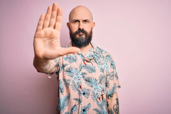 Sakallı ve dövmeli, pembe arka planda sıradan bir çiçek gömleği giyen yakışıklı kel adam avucunun içi gibi şarkı söylemeyi kesiyor. Yüzünde olumsuz ve ciddi bir jest olan uyarı ifadesi.