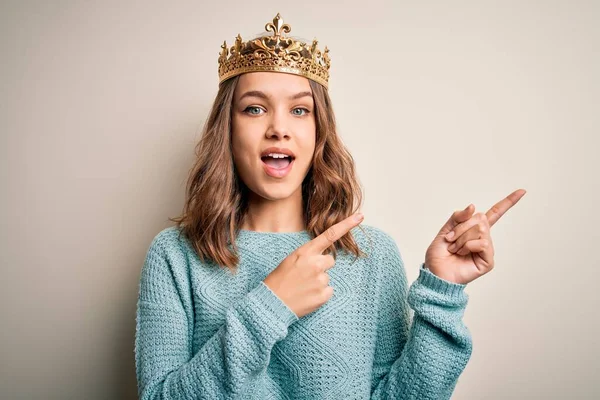 Kraliçe altın tacını takan genç sarışın kız izole edilmiş arka planda gülümsüyor ve kameraya bakıyor iki eliyle ve parmaklarıyla kenarı işaret ediyor..