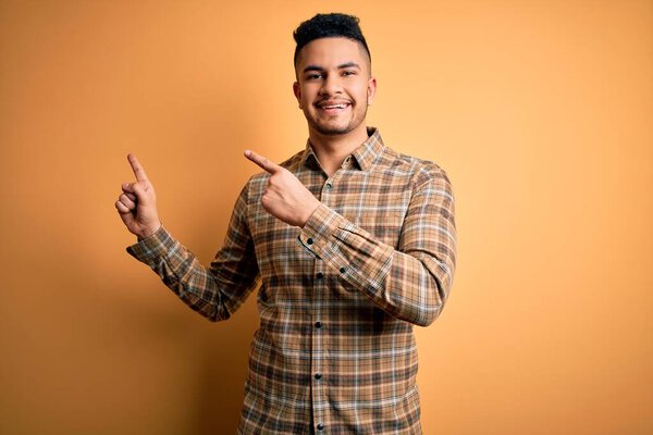 Young handsome man wearing casual shirt standing over isolated yellow background smiling and looking at the camera pointing with two hands and fingers to the side.