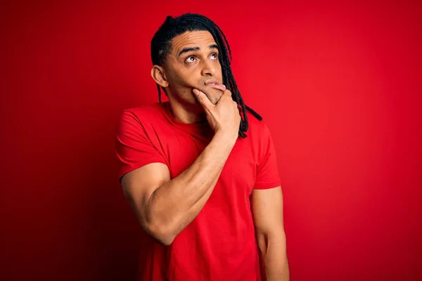 Young handsome african american afro man with dreadlocks wearing red casual t-shirt Thinking worried about a question, concerned and nervous with hand on chin
