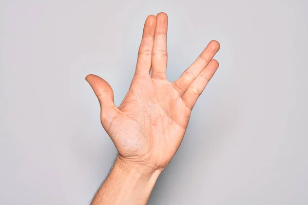 Hand of caucasian young man showing fingers over isolated white background greeting doing Vulcan salute, showing hand palm and fingers, freak culture