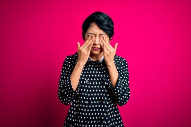 İzole edilmiş pembe arka planda dikilen sıradan bir ceket giyen genç güzel Asyalı kız yorgunluk ve baş ağrısı için gözlerini ovuşturuyor, uykulu ve yorgun bir ifade takınıyor. Görüş sorunu