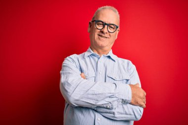 Orta yaşlı yakışıklı, beyaz, sıradan çizgili tişört giyen ve kırmızı arka planda gözlüklü mutlu yüzlü, kollarını kavuşturup kameraya bakan bir adam. Pozitif kişi.