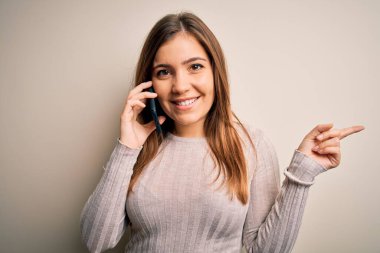 Akıllı telefondan konuşan genç bir kadın izole bir arka planda çok mutlu bir şekilde elini ve parmağını kenarı işaret ediyor.
