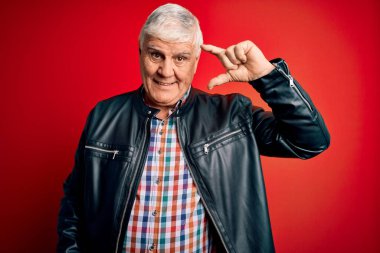 Kıdemli yakışıklı, beyaz gömlekli ve ceketli, izole edilmiş kırmızı arka planda gülümseyen ve kendine güvenen, el hareketleriyle küçük boy işareti yapan, parmakları ve kamerayı gören bir adam. Ölçü kavramı.