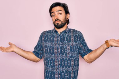 Pembe arka planda hippi tarzı giyinen yakışıklı, bohem bir adam. Kolları ve elleri havada, kafası karışmış bir ifade. Şüphe kavramı.