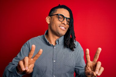 Rastgele gömlek ve gözlük takmış, gülümseyen ve parmaklarını zafer işareti yaparken gösteren genç, Afro-Amerikan bir adam. İki numara..