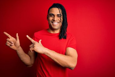 Genç, Afro-Amerikan Afrikalı, rastalı, kırmızı tişörtlü, gülümseyen ve kameraya bakan, iki eli ve parmağı yanda olan bir adam..