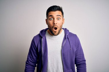 Mor eşofman üstü giyen yakışıklı genç adam izole edilmiş beyaz arka planda duruyor. Şaşırmış ve korkmuş bir ifade, korku ve heyecanlı bir yüz ifadesi var..