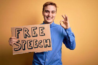 Genç ve yakışıklı kızıl saçlı adam özgürlük istiyor konuşma özgürlüğü mesajı taşıyan pankartı tutuyor parmaklarıyla imza atıyor, gülümseyerek mükemmel bir sembol oluşturuyor.