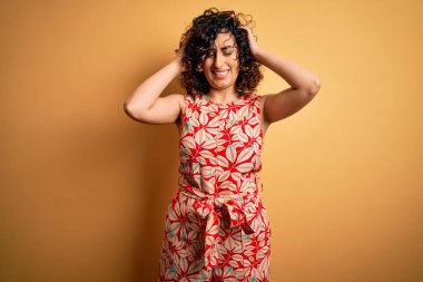 Genç ve güzel kıvırcık Arap kadın tatilde. Çiçekli bir elbise giyiyor ve güneş gözlüğü takıyor. Baş ağrısı çekiyor. Ellerini başının üstüne koy..