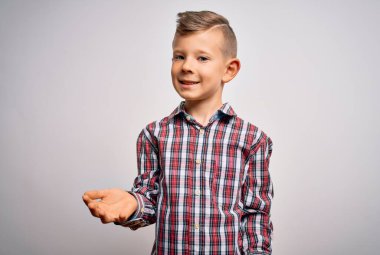 Mavi gözlü, zarif gömlekli genç, izole edilmiş arka planda neşeli gülümseyen, dostça karşılayan, olumlu ve kendinden emin bir şekilde selamlayan.