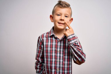 Mavi gözlü, zarif tişörtlü, soyutlanmış arka planda duran, el ve burunla işaret eden, neşeli gülümseyen küçük beyaz çocuk. Güzellik konsepti