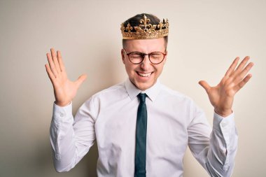 İzole edilmiş arka planda altın taç takan yakışıklı beyaz iş adamı çılgın ve başarıyı kollarını kaldırmış ve gözleri kapalı heyecanla haykırarak kutluyor. Kazanan konsept
