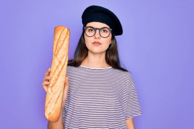 Moda Fransız beresi takmış genç güzel bir kız elinde taze ekmek ekmeği, akıllı yüzünde kendine güvenen bir ifade var ve ciddi düşünüyor.