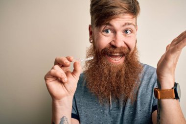 Diş düzeltmesi için dişlerini sakallı kızıl saçlı İrlandalı adam çok mutlu ve heyecanlı, kazanan yüz ifadesi zaferi büyük bir gülümsemeyle kutluyor ve ellerini kaldırıyor.