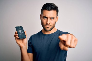 Elinde kırık ve çatlak bir akıllı telefon ekranı olan genç bir adam izole edilmiş arka planda kamerayı işaret ediyor ve sen, el işareti, ön taraftan pozitif ve kendinden emin bir hareket.