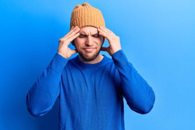 Genç, yakışıklı bir adam, günlük kazak giyiyor ve kafasında yünlü bir şapka, baş ağrısı var çünkü stres var. migren ağrısı. 