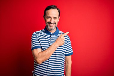Yüzünde mutlu ve doğal bir ifade olan, elleri ve parmaklarıyla yüzünü gösteren bir gülümseme ile izole edilmiş kırmızı arka planda duran, sıradan çizgili polo giyen, orta yaşlı, beyaz bir adam.