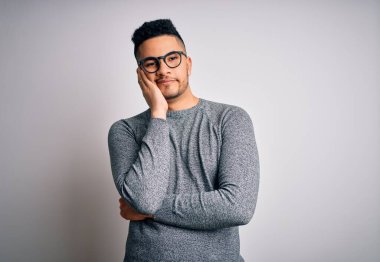 Genç, yakışıklı bir adam, gözlüklü, sıradan bir süveter ve gözlüklü, soyutlanmış beyaz arka planda yorgun ve bunalımlı görünüyor..