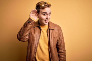 İzole edilmiş sarı arka plan üzerine sıradan deri ceket giyen genç ve yakışıklı kızıl saçlı bir adam kulağından girip kulağına fısıldayarak dedikoduları ve dedikoduları dinliyor. Sağırlık kavramı.