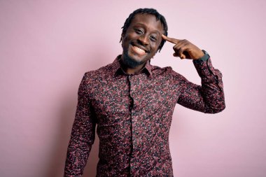 Genç, yakışıklı, Afro-Amerikalı bir adam pembe arka planda dikilmiş gülümsüyor. Tek parmağıyla, harika bir fikir ya da düşünceyle, iyi bir hafızayla.