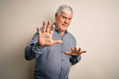 Kıdemli yakışıklı beyaz gömlekli adam izole edilmiş beyaz arka planda dikiliyor tiksindirici ve tiksindirici bir yüz ifadesi takınıyor çünkü tiksinti tepkisi veriyor. Eller havada