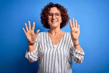 Orta yaşlı, kıvırcık saçlı, rahat çizgili tişört giyen, izole edilmiş arka planda dokuz numarayı gösteren ve gülümseyen, kendinden emin ve mutlu bir kadın..