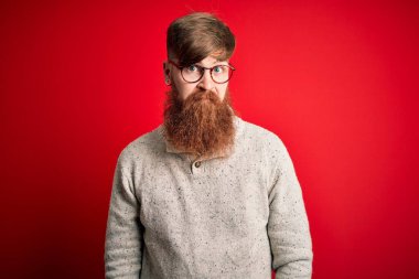 Sakallı, kızıl sakallı, kırmızı arka planda gözlük takan yakışıklı, kederli, sinirli ve korkmuş bir İrlandalı. Üzücü ifade.