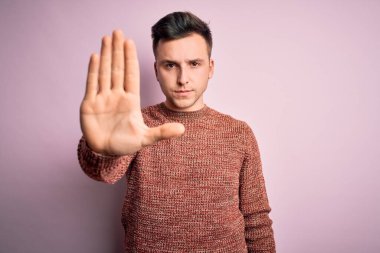 Pembe izole arka plan üzerine günlük kazak giyen yakışıklı beyaz adam avucunun içi gibi şarkı söylemeyi kesiyor. Yüzünde olumsuz ve ciddi bir jest olan uyarı ifadesi.