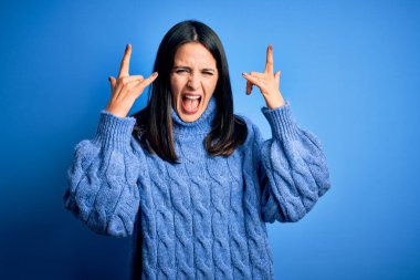 Mavi gözlü, balıkçı yaka kazak giyen, çılgın bir ifadeyle bağıran, elleri havada kaya sembolü yapan genç esmer kadın. Müzik yıldızı. Ağır müzik konsepti.