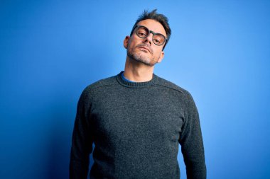 Mavi arka planda duran sıradan süveter ve gözlük takan yakışıklı genç adam yüzünde ciddi bir ifadeyle rahatlamış. Basit ve doğal bir şekilde kameraya bakıyorsun..