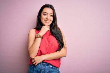 Genç esmer kadın pembe izole edilmiş arka plan üzerine gündelik bir tişört giyerek kameraya bakıyor kollarını kavuşturup ve çenesini kaldırarak gülümsüyor. Olumlu düşünüyorum..