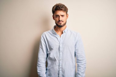Beyaz arka plan üzerinde duran çizgili gömlekli genç yakışıklı adam uykulu ve yorgun görünüyor, yorgunluktan yorgun ve akşamdan kalma, sabahları tembel gözler..