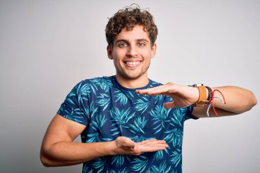 Sarışın, yakışıklı, tatilde. Kıvırcık saçlı, sıradan bir tişört giyiyor. Ellerinde kocaman ve büyük beden işareti olan bir işaret var. Kameraya bakıp gülümsüyor. Ölçüm konsepti.