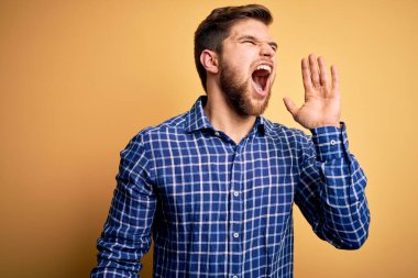 Sarışın, sakallı ve mavi gözlü genç bir işadamı sarı arka planda tişört giyip el ele tutuşarak bağırıyor ve bağırıyordu. İletişim konsepti.