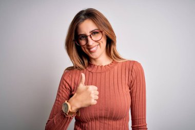 Genç, güzel, esmer bir kadın, beyaz arka planda gözlüklü, sıradan bir süveter giyiyor ve el hareketleriyle mutlu bir jest yapıyor. Kameraya bakıp başarıyı gösteren ifade onaylanıyor.