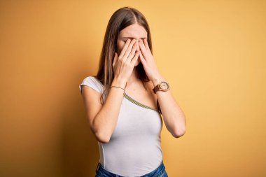 İzole edilmiş sarı arka plan üzerine gündelik tişört giyen genç, güzel bir kızıl kadın yorgunluk ve baş ağrısı için gözlerini ovuşturuyor, uykulu ve yorgun bir ifade takınıyor. Görüş sorunu