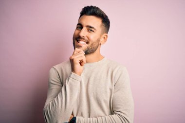 İzole edilmiş pembe arka plan üzerinde duran sıradan bir süveter giyen genç yakışıklı kameraya kollarını kavuşturup gülümseyerek ve çenesini kaldırarak bakıyor. Olumlu düşünüyorum..