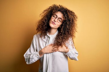 Kıvırcık saçlı, piercingli, tişörtlü, gözlüklü, göğsünde elleri kapalı, yüzünde minnet ifadesi olan genç ve güzel bir esmer kadın. Sağlık kavramı.