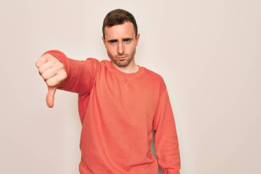 Mavi gözlü, sıradan bir süveter giyen, beyaz arka plan üzerinde duran, mutsuz ve sinirli, reddedilmiş ve olumsuz bir hareket yapan genç bir adam. Kötü ifade.