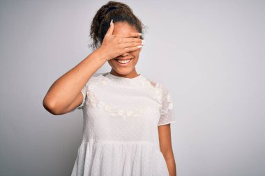Genç, güzel, Afro-Amerikalı bir kız, beyaz arka planda dikilen günlük tişörtler giyiyor, gülümsüyor ve yüzünde şaşkınlıktan gözleri kapayarak gülüyor. Kör kavram.