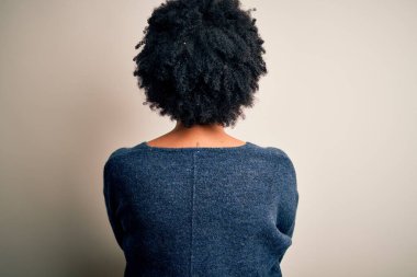 Kıvırcık saçlı, sıradan bir kazak giyen, kollarını kavuşturup arkaya bakan güzel Afro-Amerikan kadın.